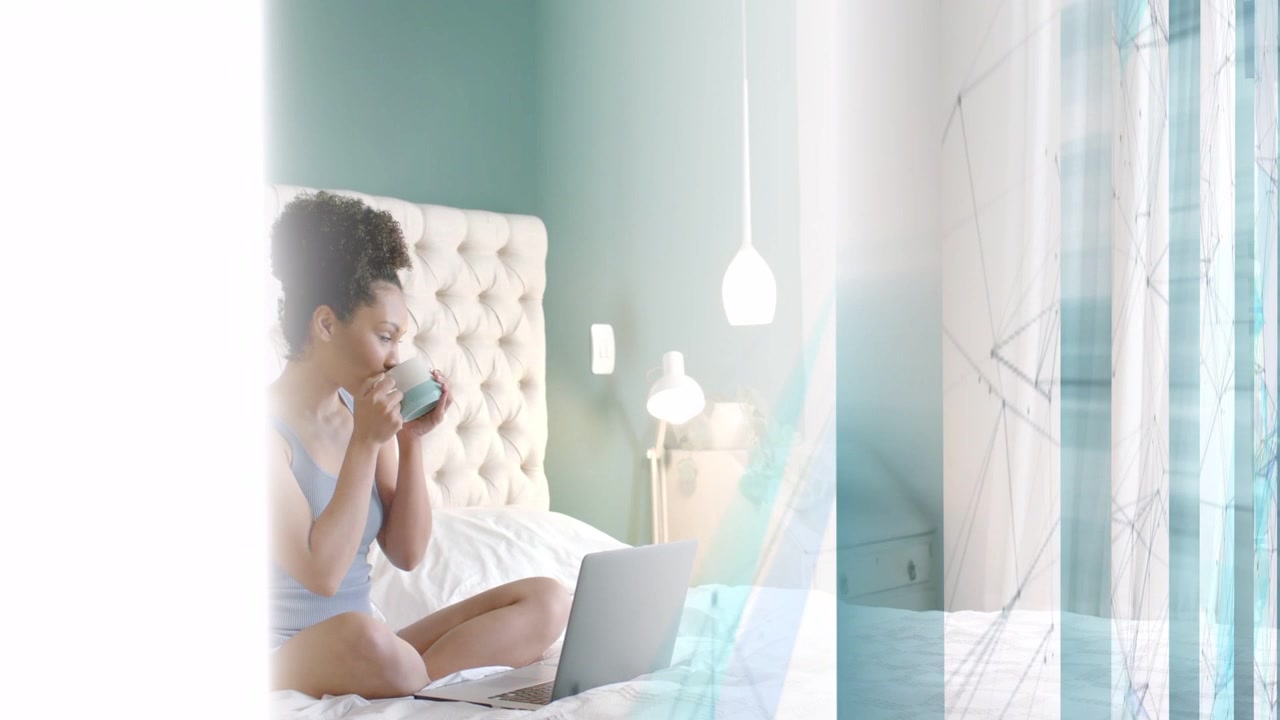 Donna seduta sul letto, che sorseggia da una tazza e guarda il laptop, con una sovrapposizione blu che si sposta, mentre lavora da remoto