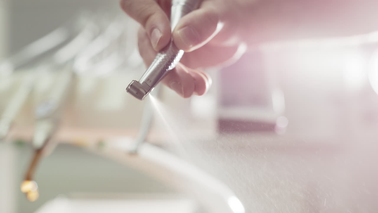 Water sprayed from dental tool held by caucasian hand in clinic, closeup backlit