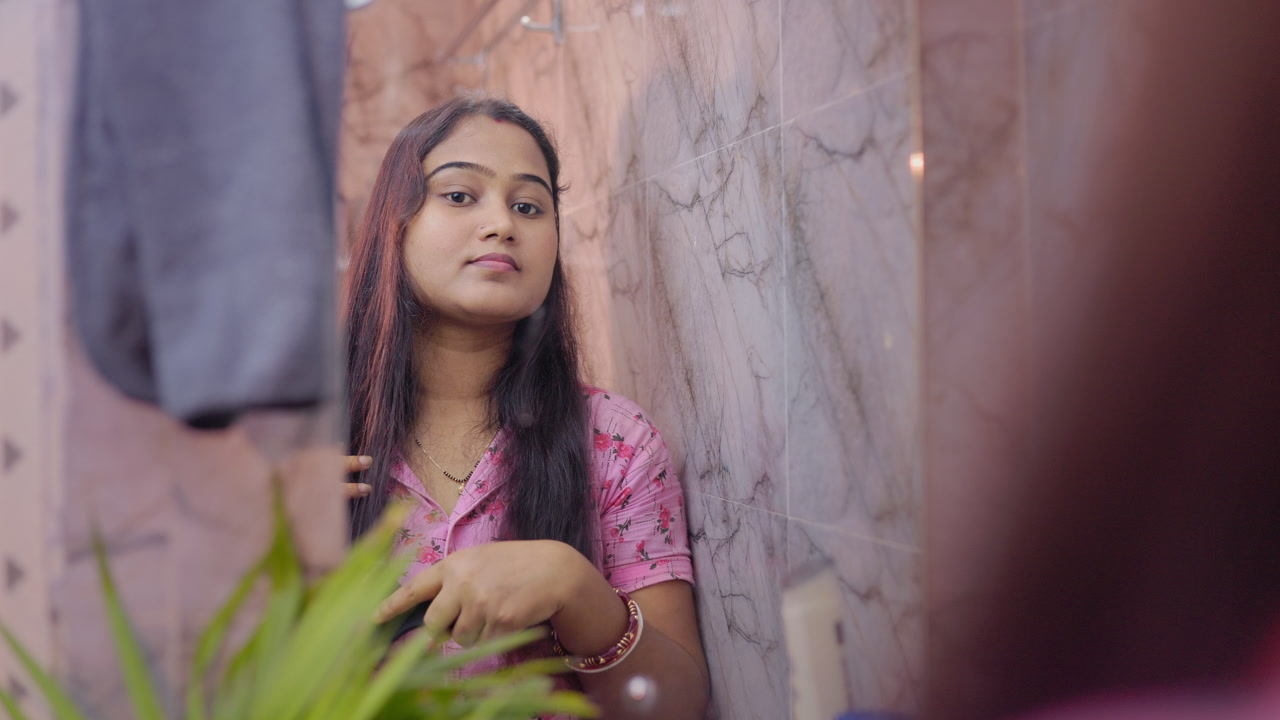 women haircare, Indian woman combing her hair with a comb and looking her reflection in the bathroom mirror
