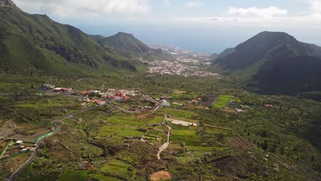 Dolly-back,-view-at-village,-road,-green-landscape-and-majestic-towering-mountains-on-sides