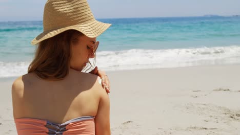 vista trasera de una mujer caucásica aplicando loción en su cuerpo en la playa 4k
