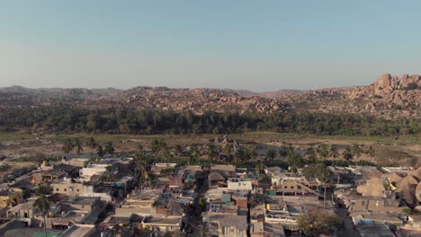 Borde-De-La-Ciudad-De-Hampi-Con-Edificios-Antiguos-Que-Contrastan-Con-El-Paisaje-Rocoso-En-Karnataka,-India---Toma-Panorámica-Aérea