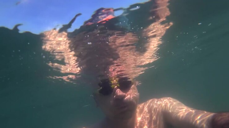 Person swimming underwater looking towards the bright sun shining through the surface, creating beautiful light patterns