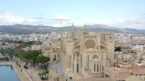 AERIAL:-Close-Up-over-Palma-Cathedral-in-Daylight,-Blue-Sky-with-Traffic-and-Tourists-on-Tropical-Island-Mallorca,-Spain-on-Sunny-Day-Vacation,-Travel,-Sunny