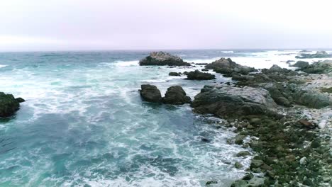 Felsiger-Monterey-Kalifornien-Strand-Mit-Krachenden-Wellen-Und-Vögeln,-Die-In-Zeitlupe-Fliegen-Und-Sich-Einer-Großen-Felsformation-Nähern