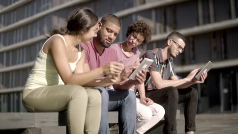 cheerful colleagues using modern devices on street.