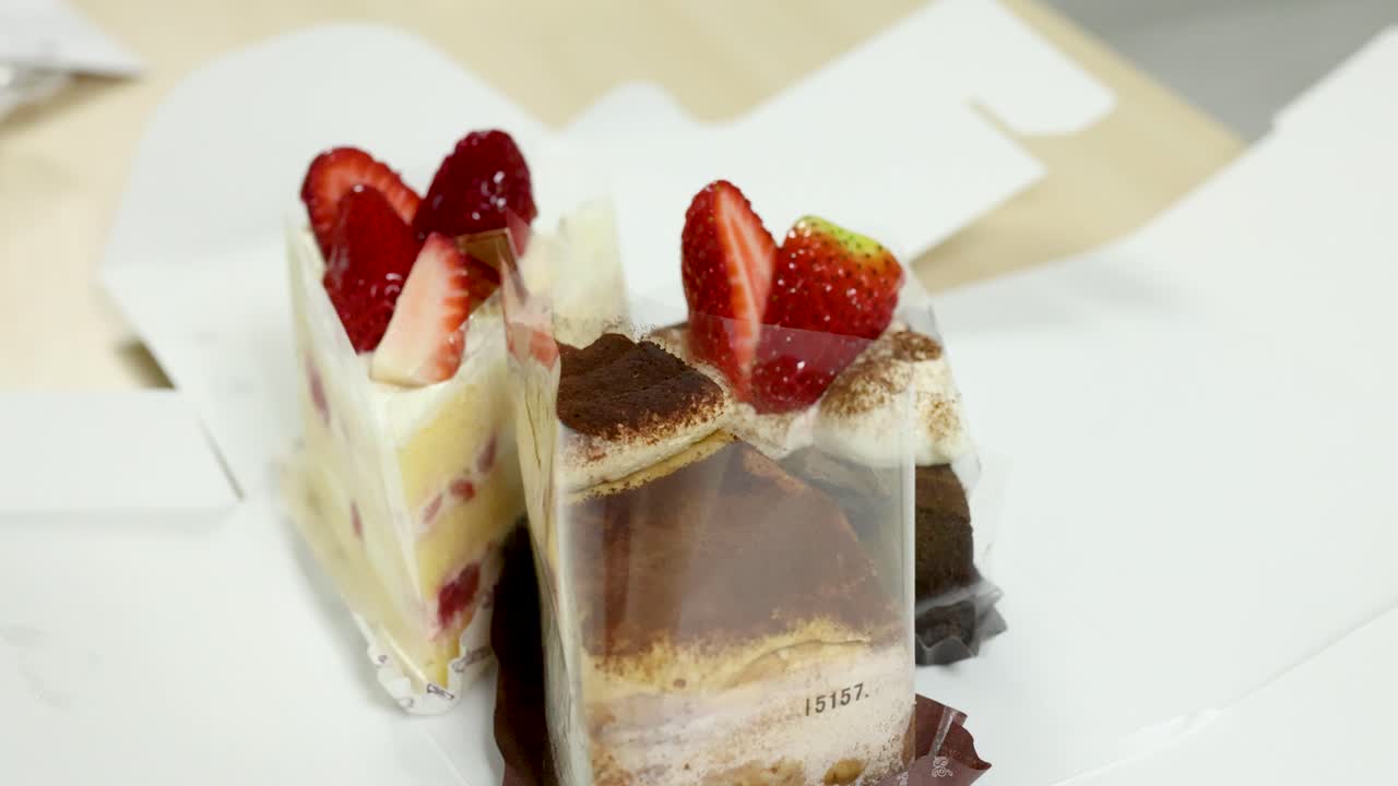 Two gourmet cake slices with strawberries in a white bakery box under soft indoor lighting