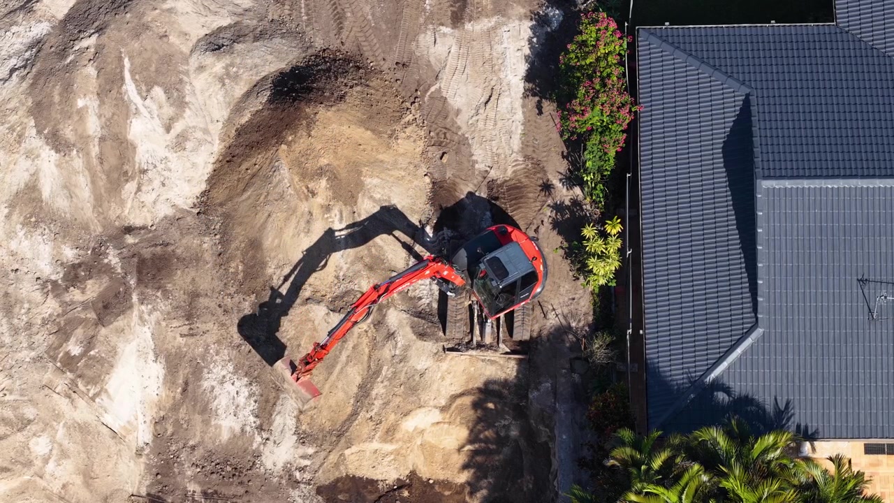 Droneoptagelse ovenfra af rødt maskineri, der flytter jord til renovering af baghave i klart dagslys.