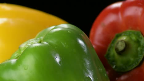 pimientos frescos verduras amarillas, rojas y verdes girando sobre un fondo negro