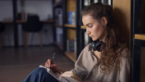 students sitting against bookshelf writing notes into notepad