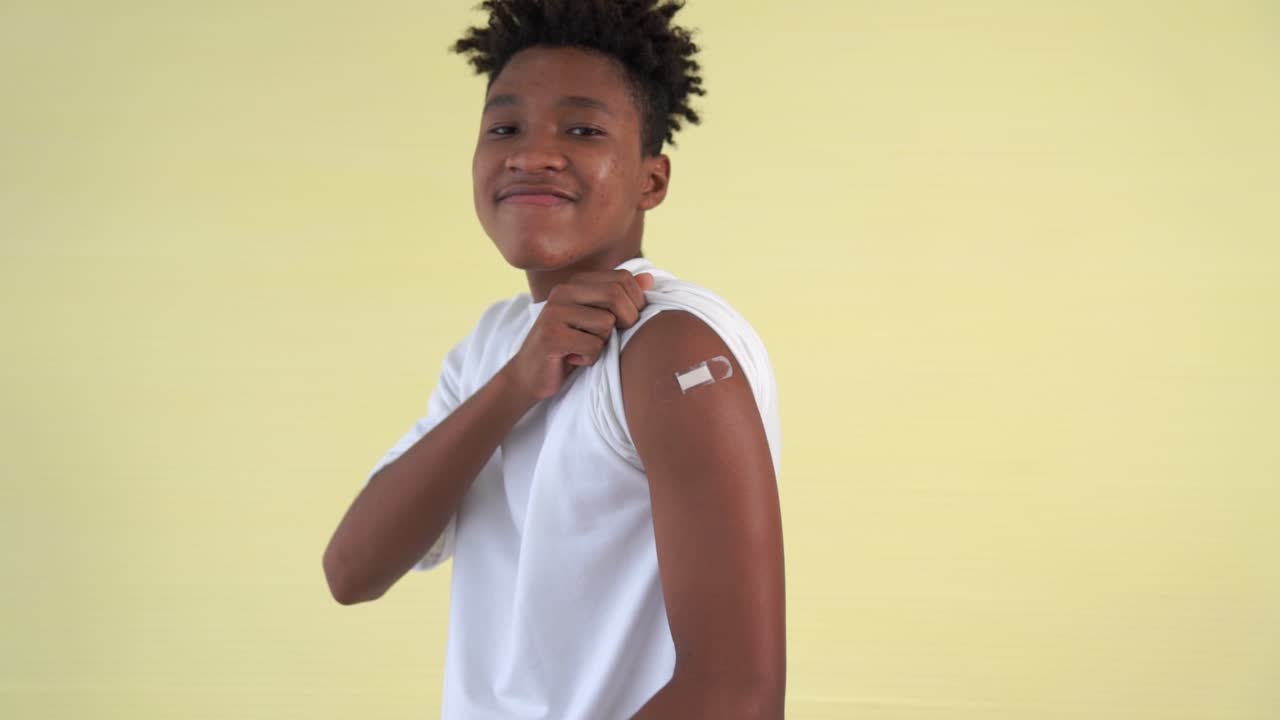 African American teenager showing COVID-19 vaccine bandage merrily