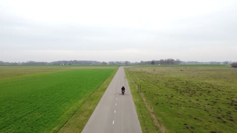 drone shot following motorcyclist driving towards the city in between grass fields