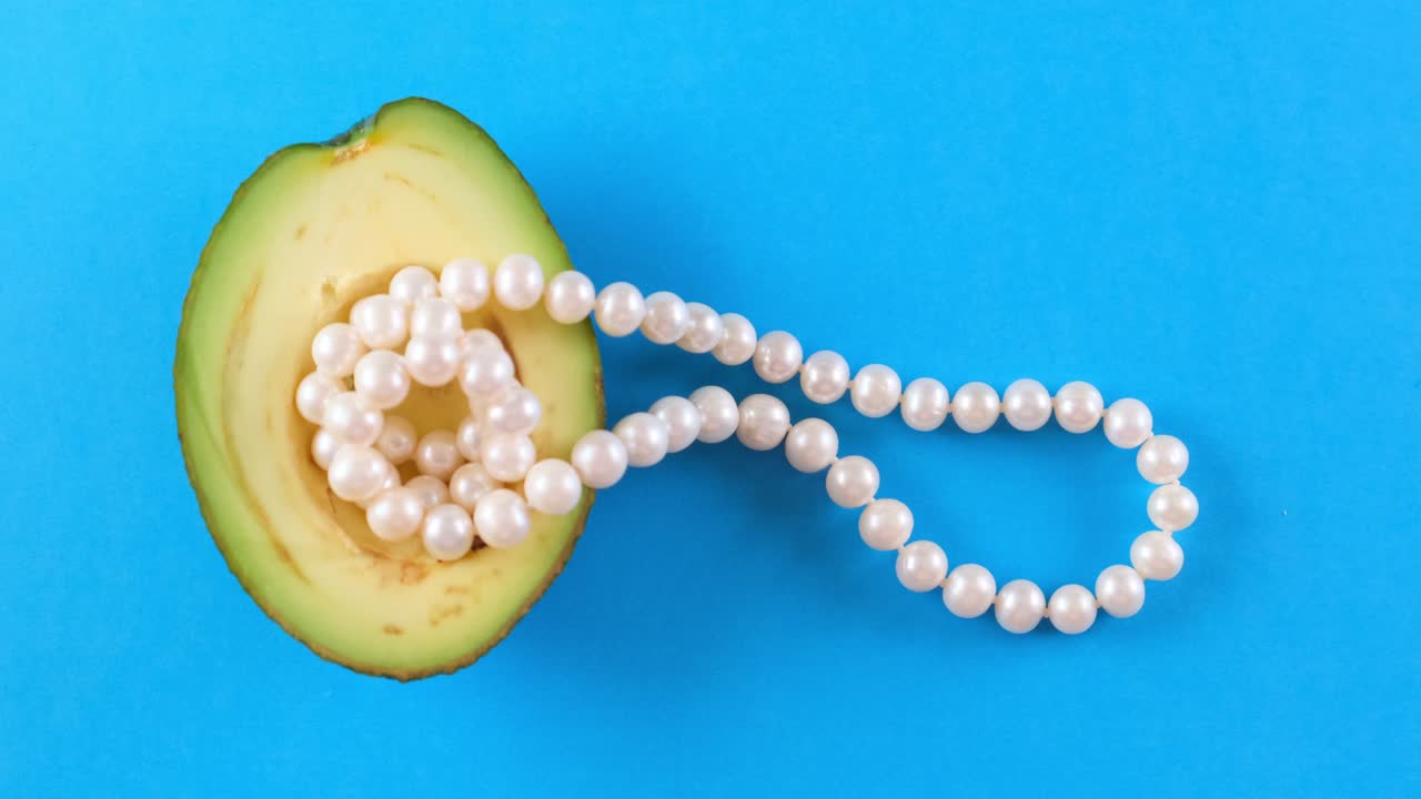 파란색 배경에 진주와 함께 반 신선한 아보카도 과일.