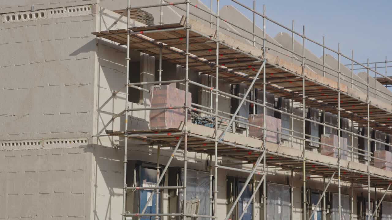 Slow tilt up of scaffolds put up against houses under construction in a newly developed suburban neighborhood
