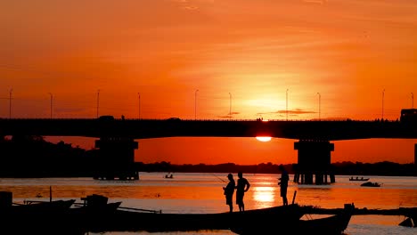 sunset silhouette of people fishing under a bridge