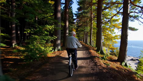 senior man cycling through autumn forest path by the coast