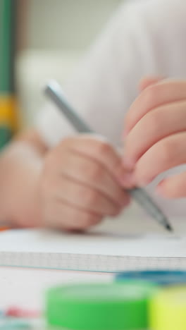 toddler student draws with marker in exercise book at table closeup. little boy colours picture on notebook page at art lesson in elementary school