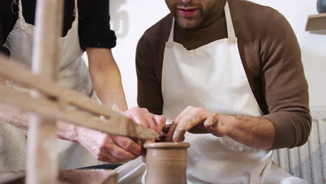 Close-Up-Of-Male-Teacher-Helping-Man-Sitting-At-Wheel-In-Pottery-Class