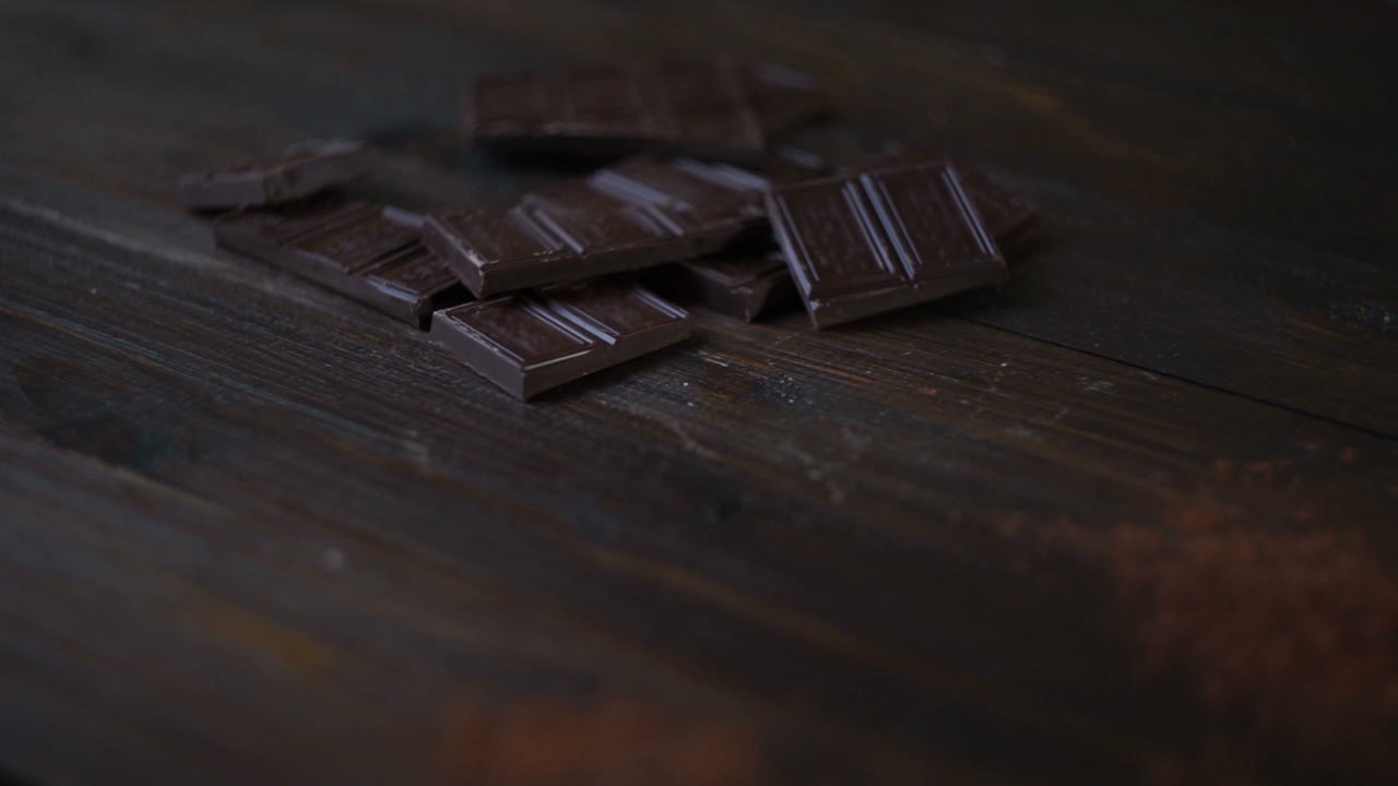 barra de chocolate oscuro. polvo de cacao en una taza de vidrio sobre un fondo de madera