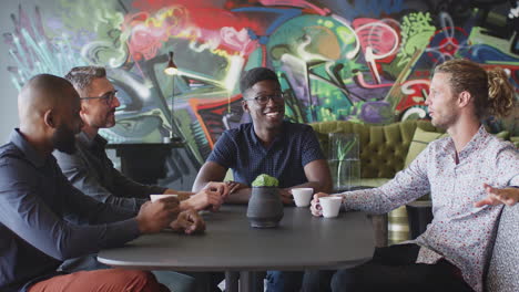 four male creative colleagues talking at a table in their workplace canteen, close up