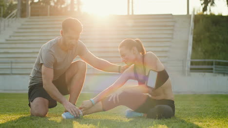 Junge-Joggerin,-Die-Auf-Grünem-Gras-Sitzt-Und-Schmerzen-Im-Bein-Hat,-Die-Während-Des-Trainings-Im-Stadion-An-Einem-Sonnigen-Tag-Verletzt-Wurden