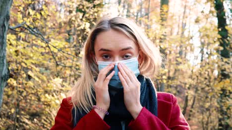 retrato de una joven hermosa mujer poniéndose una máscara de seguridad corona en medio de un bosque otoñal marrón anaranjado mientras usa un abrigo rojo versión 5