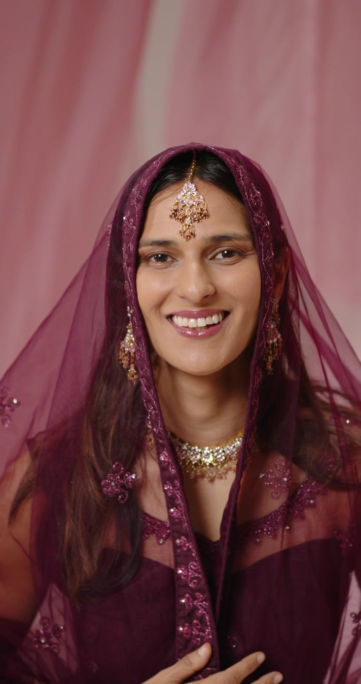 Vertical video: Indian woman holding dupatta, posing in studio, sliding veil revealing maang tikka