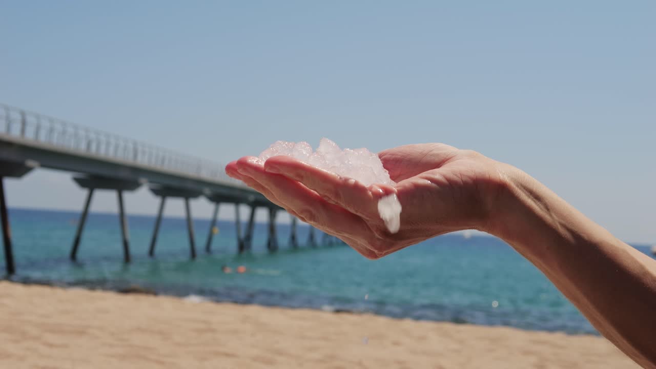 Ice cubes melting in hand on a beach