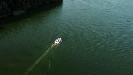 Small-motor-boat-driving-on-a-lake-next-to-a-forest-in-Brandenburg,-Germany