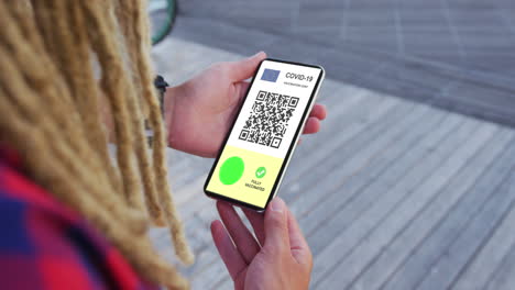 hombre con dreadlocks sosteniendo un teléfono inteligente, certificado de vacunación contra la covid, bandera de la ue y código qr en la pantalla