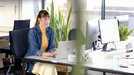 typing on laptop, woman working in modern office with plants and desk accessories