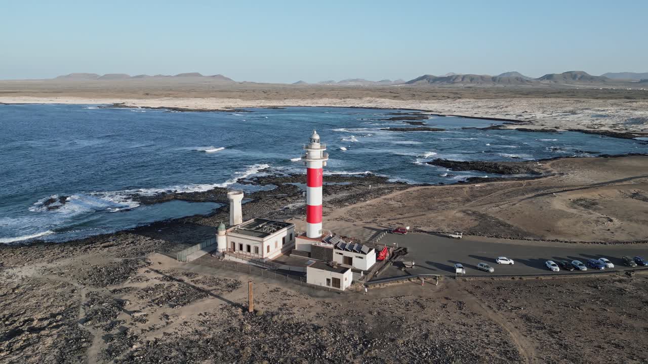 Drone footage of El Tostón Lighthouse from the side in El Cotillo, Fuerteventura, showing volcanic rocks and Atlantic shoreline.