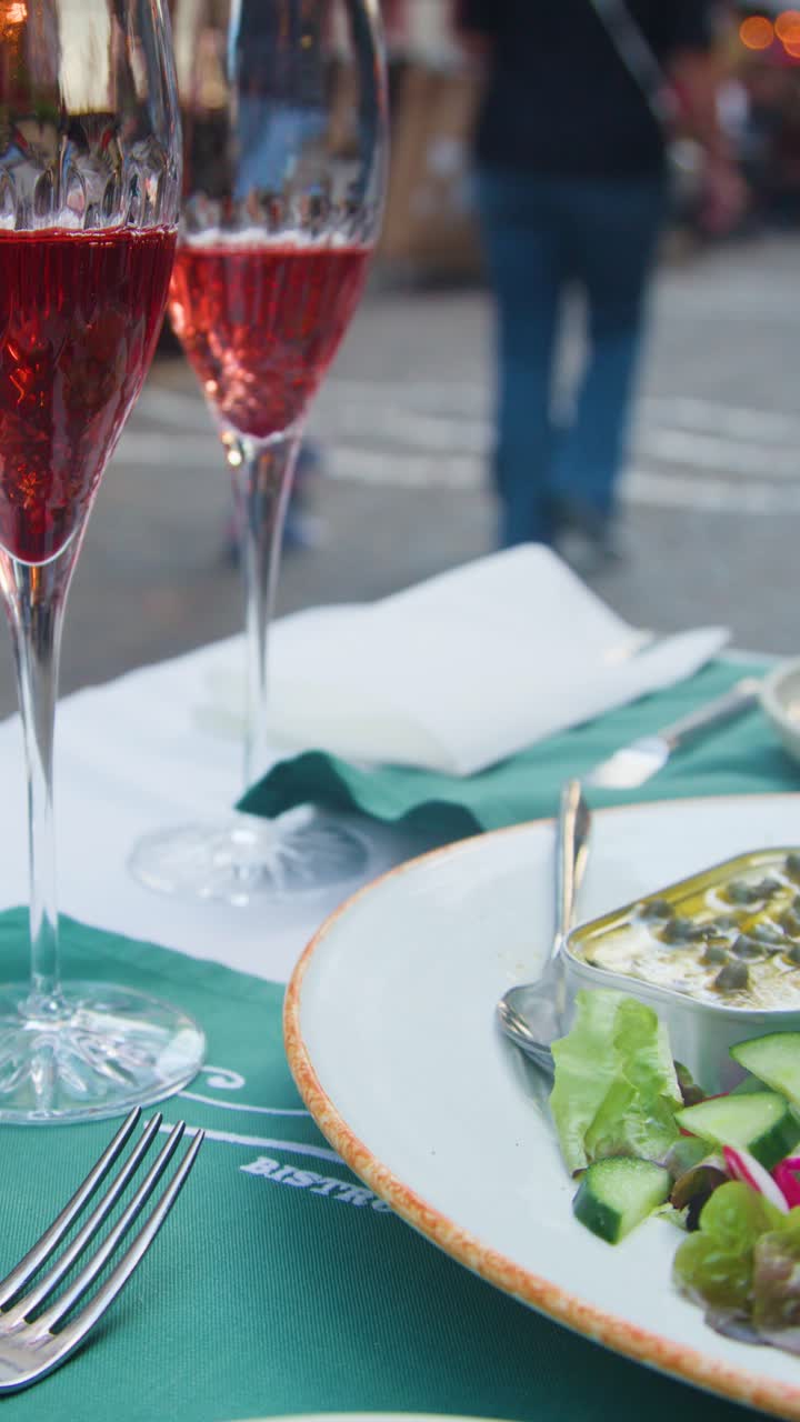Salad plate and cocktails on outdoor cafe table, blurred people walking, soft evening lighting