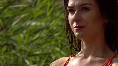 closeup of the face of a young woman who is lit by the sun, she is standing against a green natural background