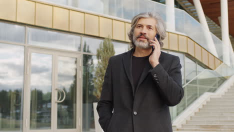 senior man on phone call outside modern office building