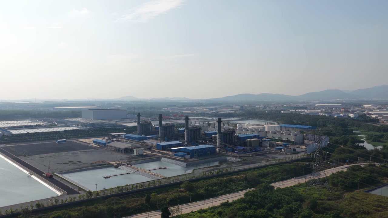 Sweeping aerial footage showing a large power plant with towering smokestacks, surrounded by water reservoirs and a vast industrial complex on a hazy day, illustrating energy production