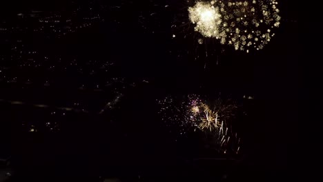 toma aérea de fuegos artificiales con luces de la ciudad en el fondo