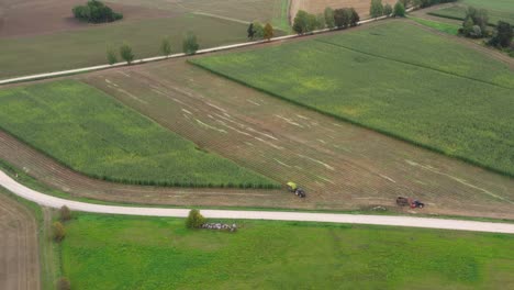 Silage-harvesting-season,-two-tractors-with-trailers-on-field,-aerial-panorama-view