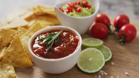 Close-up-of-nachos-and-sauces-on-wooden-tray-on-black-surface