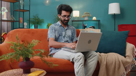 Smiling-indian-man-counting-money-cash-and-use-laptop-pc-calculate-domestic-income-earnings-at-home