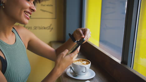 cliente femenina en la ventana de una cafetería enviando mensajes usando un teléfono móvil