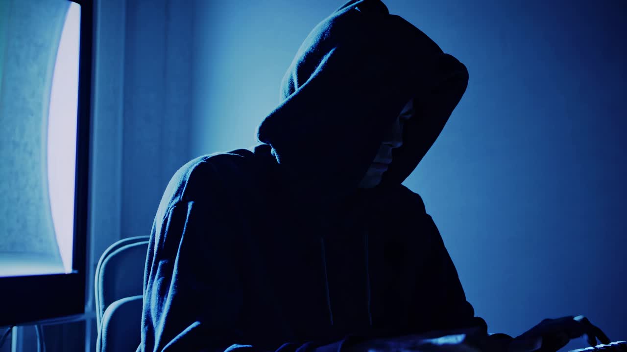 A moody, low-angle video shot of a hooded figure in a dimly lit room, highlighting mystery
