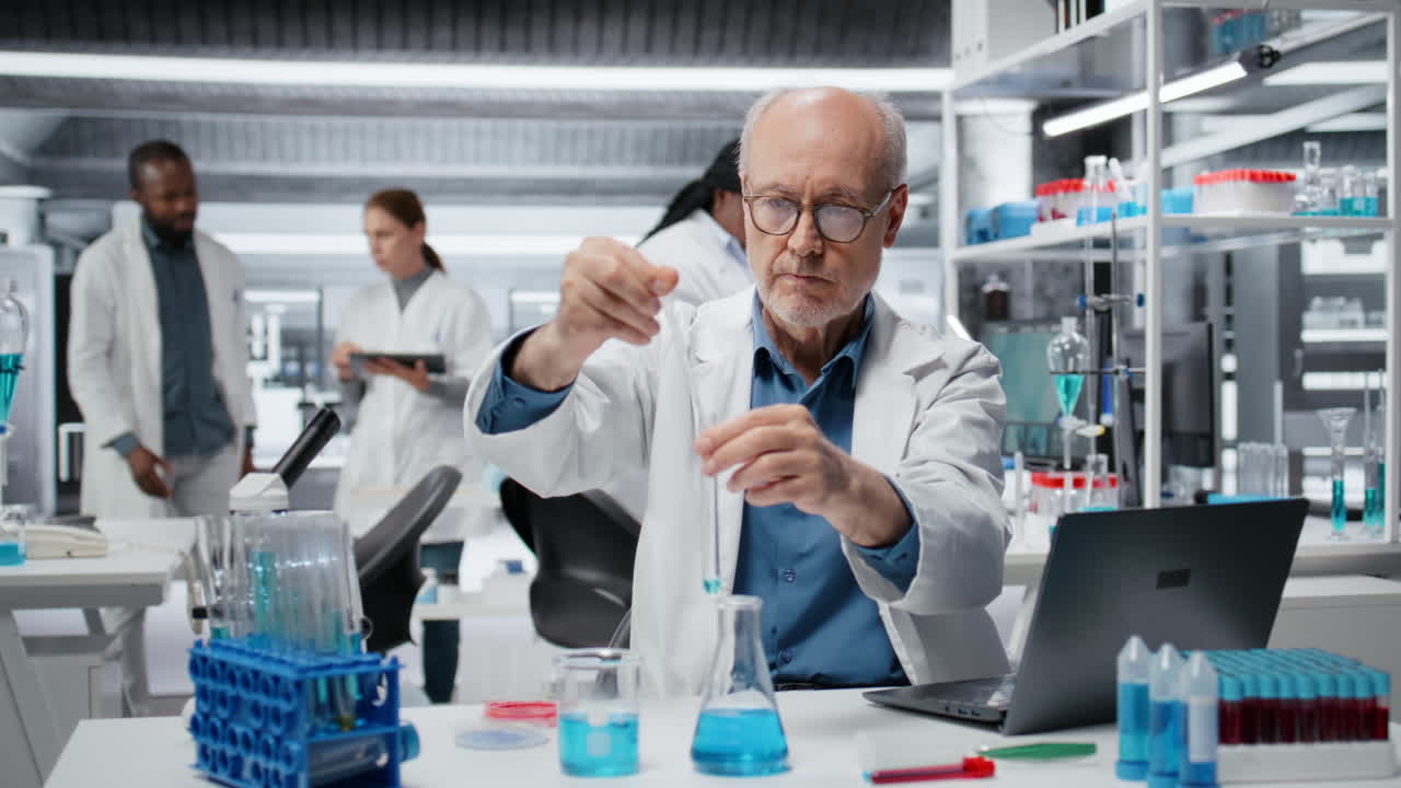 Elderly researcher inspecting blue liquid clarity in test tube, using laptop