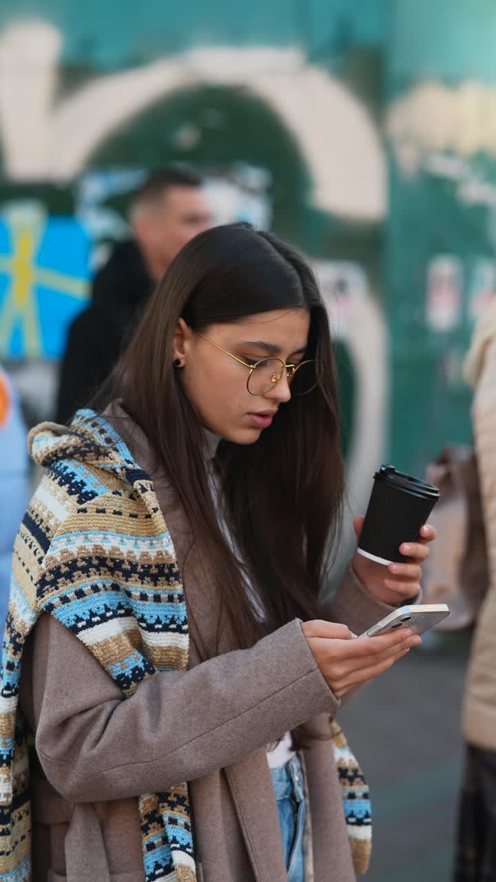mujer joven usando un teléfono inteligente mientras bebe café al aire libre