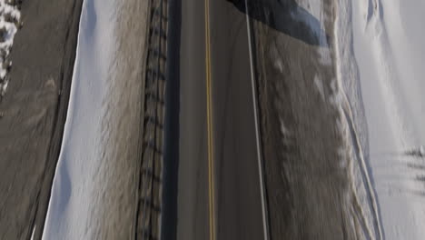 aerial tilting shot of a car driving through the rocky mountains