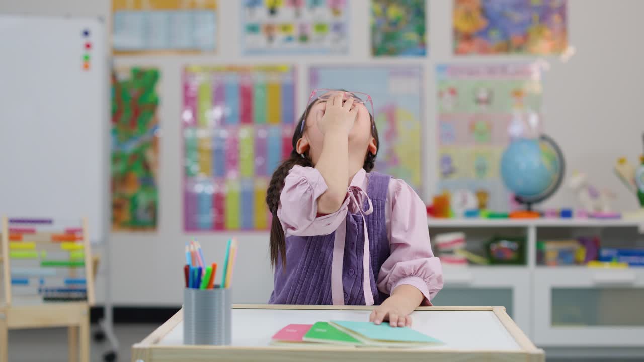 Cheerful Asian schoolgirl laughs at classroom desk, bright lighting, static camera, colorful educational background