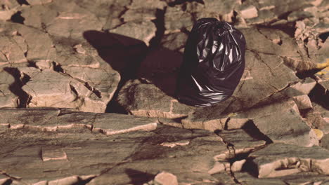 black trash bag lay on a rocky beach