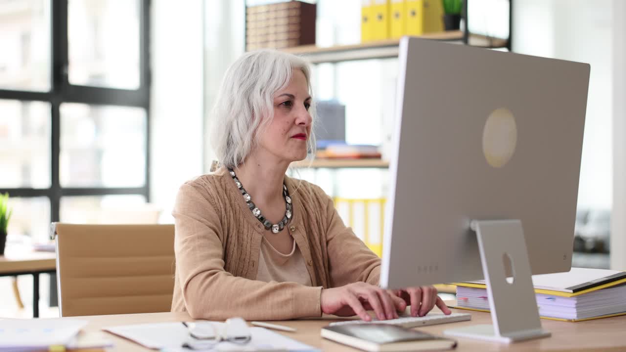 Ernsthafter älterer Mitarbeiter arbeitet am Computer am Schreibtisch im Büro.
