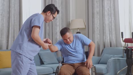 asian male nurse holding patient's hand who in a wheelchair to stand up and walk during a physical therapy at home