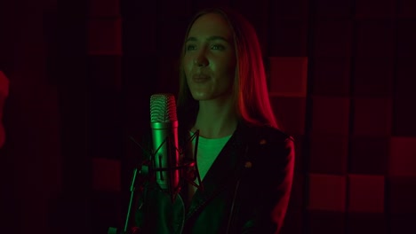 una mujer atractiva canta en un micrófono a la luz del neón en el estudio oscuro. una chica emocional está grabando una canción en un fondo negro